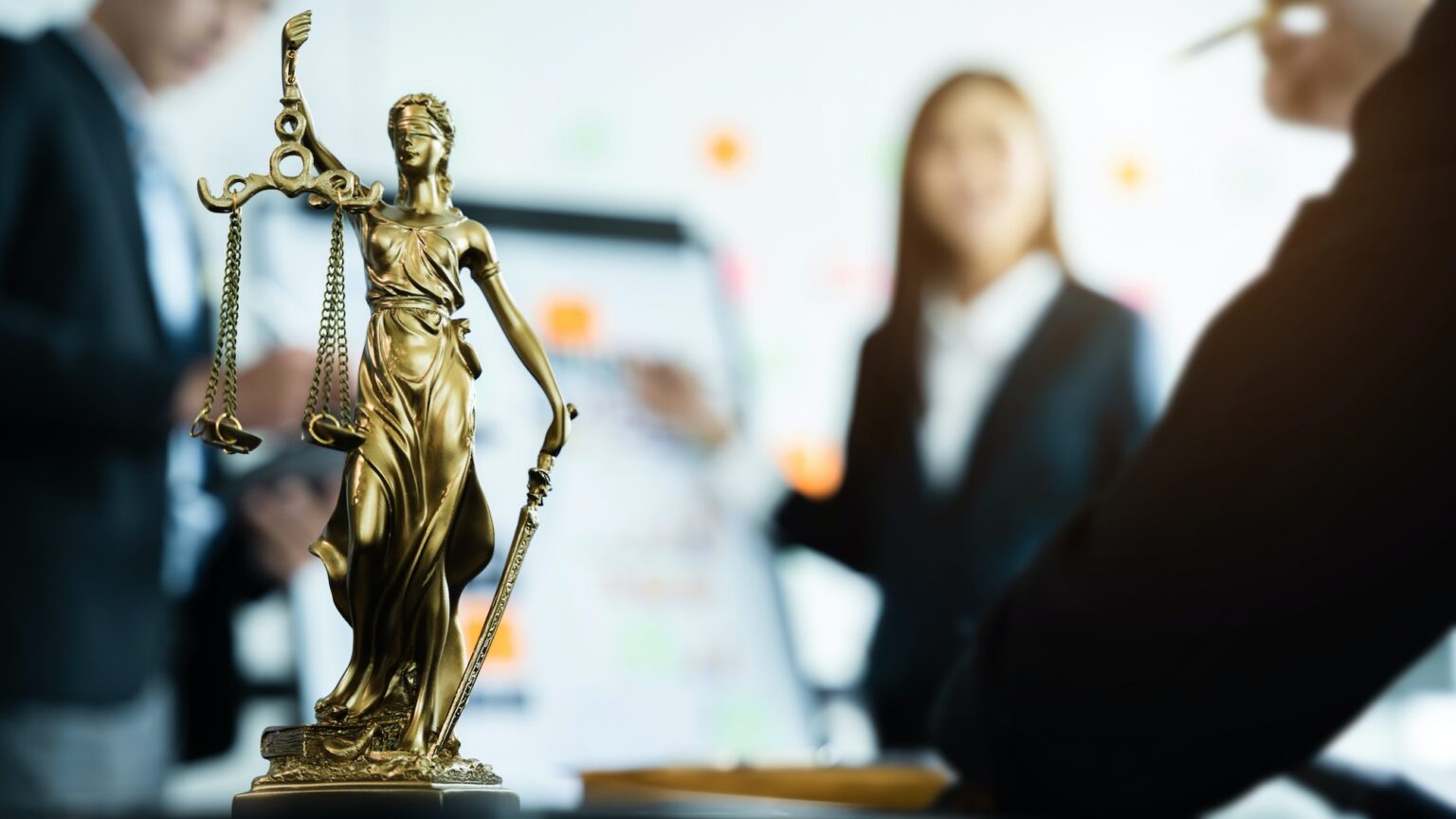 Statue of justice with scales, the team meeting at the law firm behind the concept of in office law.
